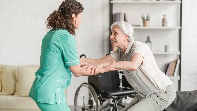 Une soignante aide une femme en fauteuil roulant à se lever.