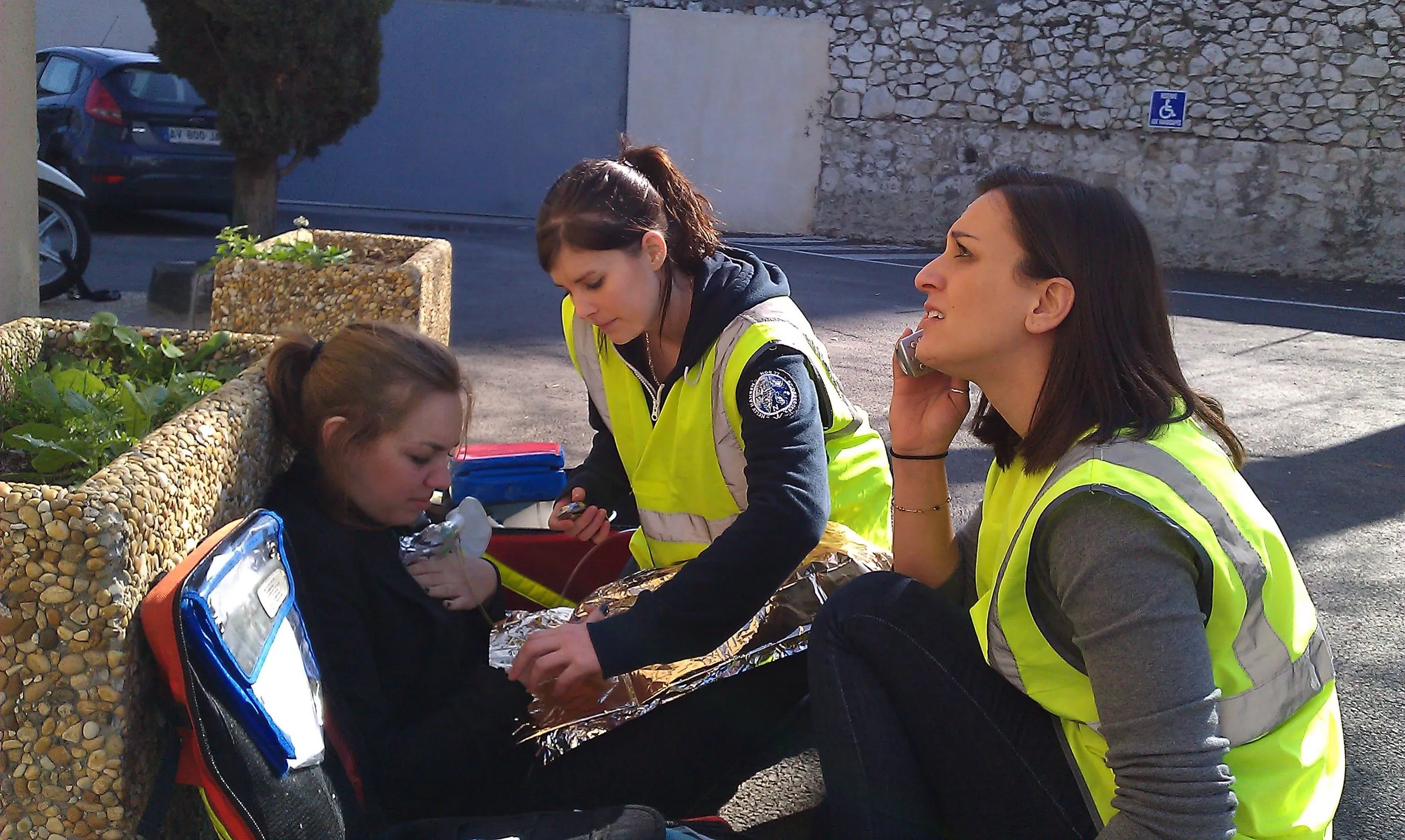 Trois secouristes en gilet jaune prennent en charge une victime assise au sol lors d'un exercice.