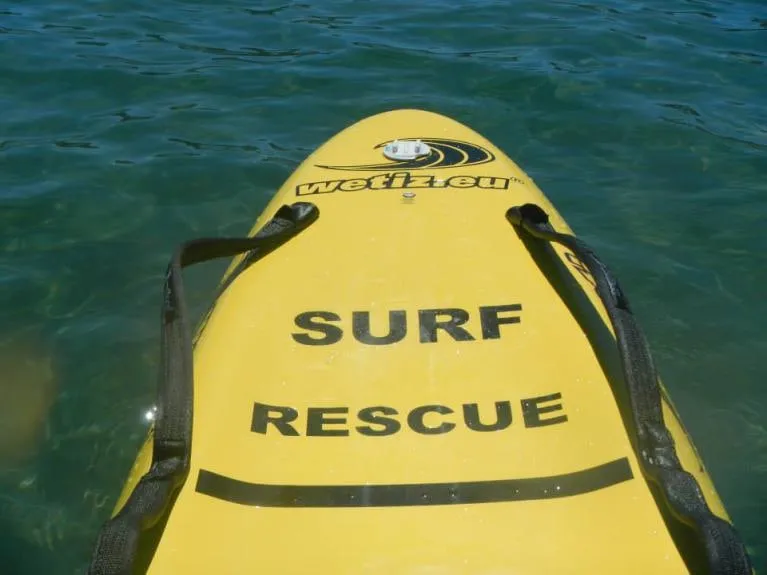 Une planche de sauvetage jaune marquée Surf Rescue flotte sur l'eau.