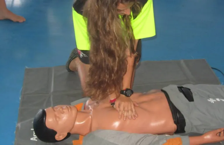 Une stagiaire en gilet jaune pratique le massage cardiaque sur un mannequin.