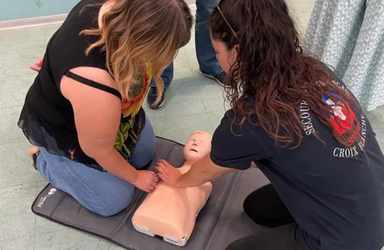 Deux stagiaires en tee-shirt Croix Blanche pratiquent le massage cardiaque sur un mannequin.