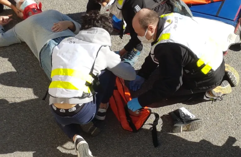 Deux secouristes en gilet prennent en charge une victime allongée au sol, sac de secours ouvert.