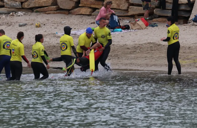 Un groupe de stagiaires en tee-shirt jaune s'entraîne au bord de l'eau.